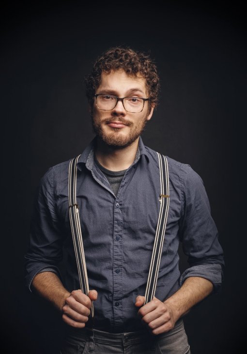 Adrian Goldner mit Brille und Hosenträgern vor dunklem Hintergrund, er schaut in die Kamera