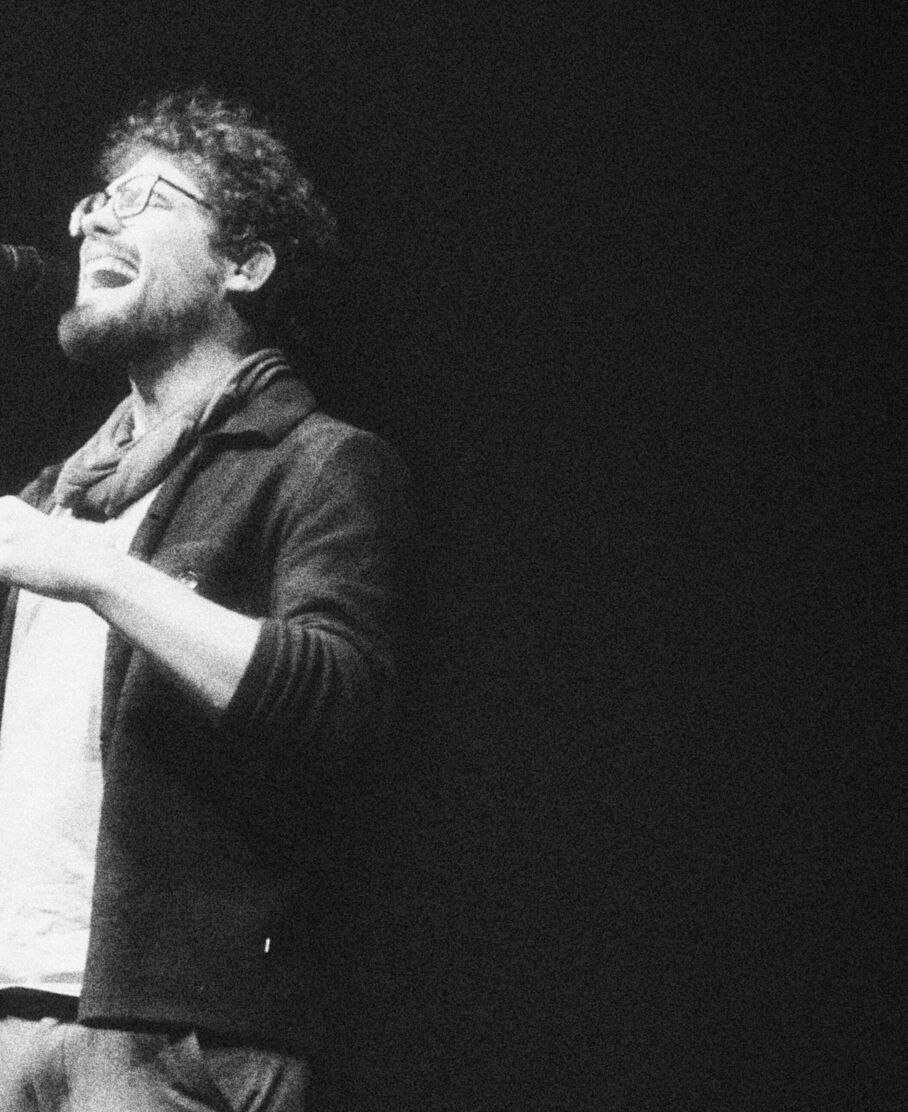 Schwarzweißfoto von Adrian Goldner, der mit offenem Mund in ein Mikrofon singt